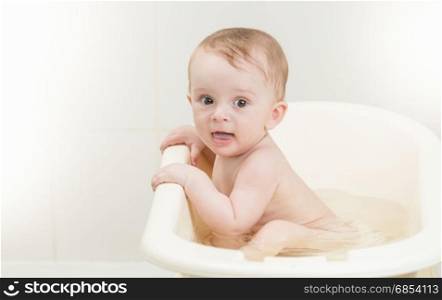 Adorable baby boy with foam on head having bath time