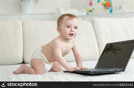 Adorable baby crawling on bed to the laptop