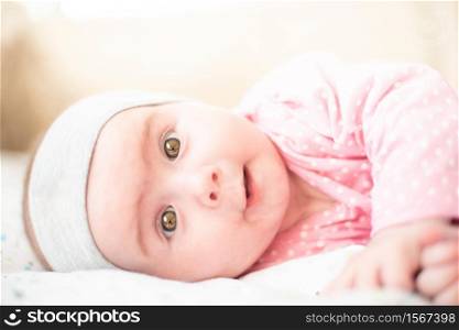 Adorable baby girl in pink lie on side and looking towards camera and smiling. Copy space on top. 6 months old baby. Adorable baby girl in pink lie on side and looking towards camera and smiling. Health concept