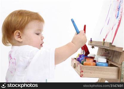 Adorable Baby Girl Painting At Easel. Shot over white background.