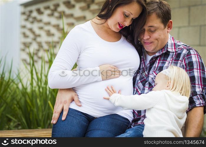 Adorable Baby Girl Puts Her Hand On Stomach of Mommy As Daddy Looks On.
