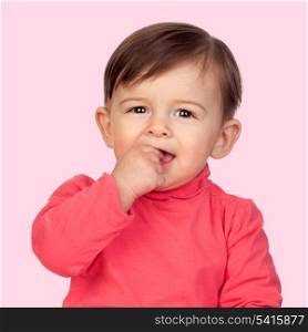 Adorable baby girl with her hand in mouth isolated on pink background