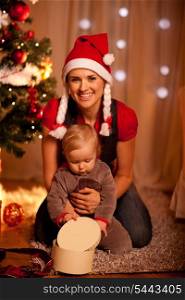 Adorable baby near Christmas tree opening Christmas gifts with mother&#xA;