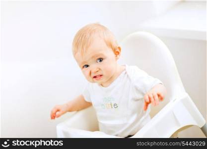 Adorable baby sitting in baby chair and making funny face&#xA;