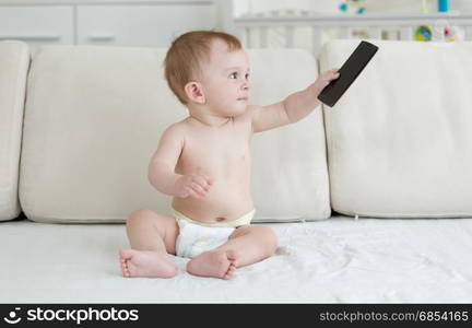 Adorable baby sitting on bed and playing with smartphone