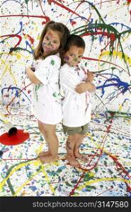 Adorable boy and girl covered in paint standing on splattered paint background, full body