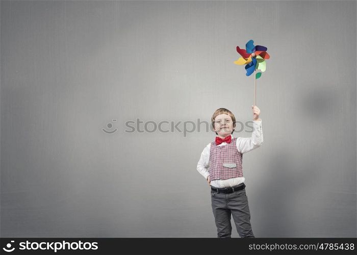 Adorable boy with windmill on cement background. Careless happy childhood