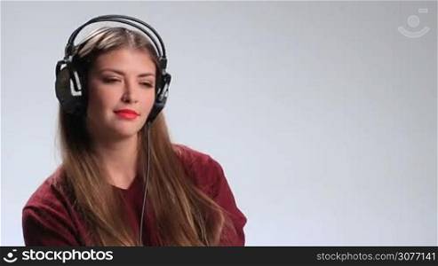 Adorable brunette girl wearing red lipstick and enjoying the track on the radio with headphones. Sexy young woman with long hair looking at the camera playfully and seductively touching her red lips with finger while listening music in earphones.