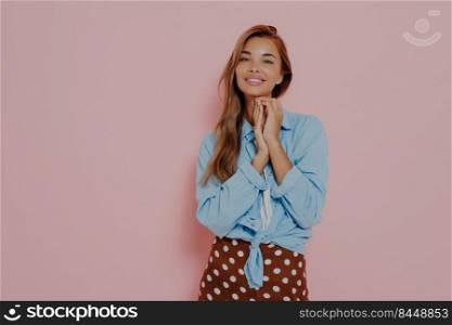 Adorable caucasian lady keeping palms together in beautiful face, expressing delight and touched by complement, being excited before date while standing against pink background with copy space. Adorable lady expressing delight on pink background