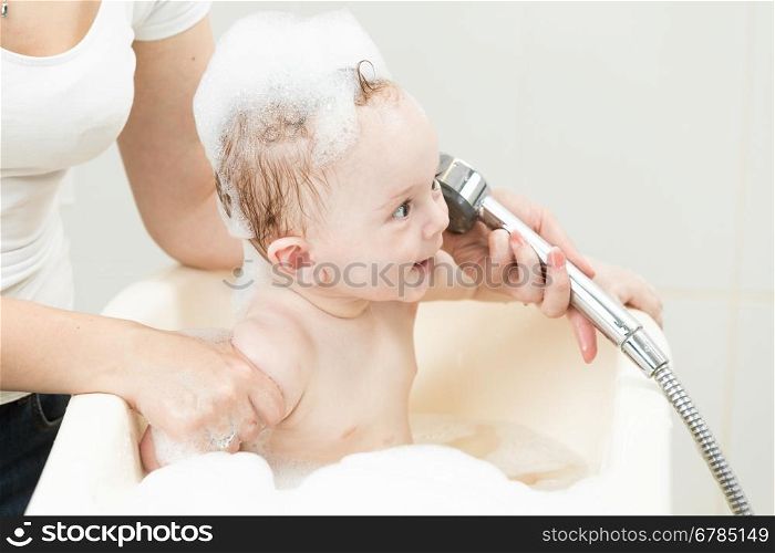 Adorable cheerful baby boy having bath and playing with shower head