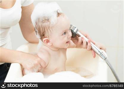 Adorable cheerful baby boy having bath and playing with shower head