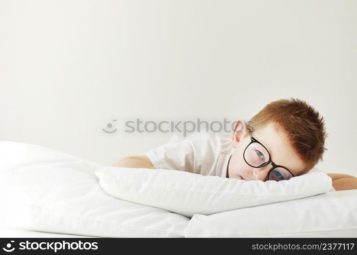 Adorable child boy in glasses is lying in bed. morning dreaming on white bed. Adorable child boy in glasses is lying in bed. morning dreaming on white bed.