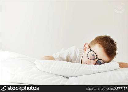 Adorable child boy in glasses is lying in bed. morning dreaming on white bed. Adorable child boy in glasses is lying in bed. morning dreaming on white bed.