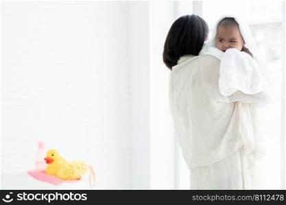 Adorable cold African newborn baby was in mother"s embrace after bathing in bathtub. Asian young mother wrap up her little daughter warm in towel at bathroom. Newborn baby cleanliness care concept