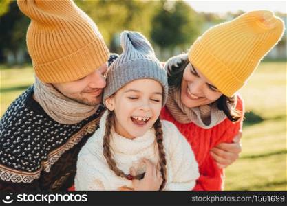 Adorable funny small kid has fun with parents who look at her with great love, enjoy spending free time together, admire beautiful nature and fresh air. People, happiness and childhood concept