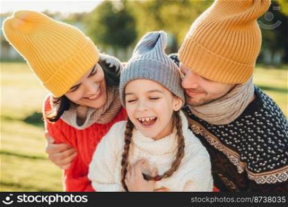 Adorable funny small kid has fun with parents who look at her with great love, enjoy spending free time together, admire beautiful nature and fresh air. People, happiness and childhood concept