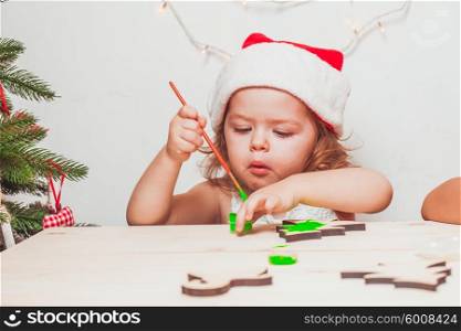 Adorable girl is painting wooden Christmas figurines. Handmade Christmas decorations
