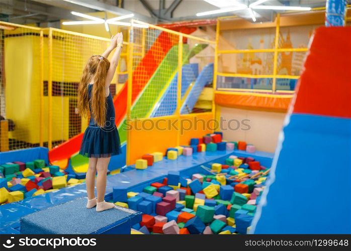 Adorable girl jumping on kids trampoline, playground in entertainment center. Play area indoors, playroom. Adorable girl jumping on kids trampoline