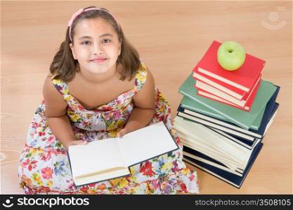 Adorable girl with many books reading on wooden floor