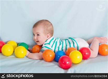 Adorable happy baby boy with multicolored balls on blue background