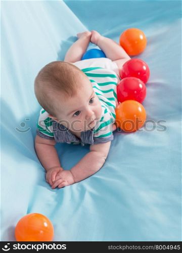 Adorable happy baby boy with multicolored balls on blue background