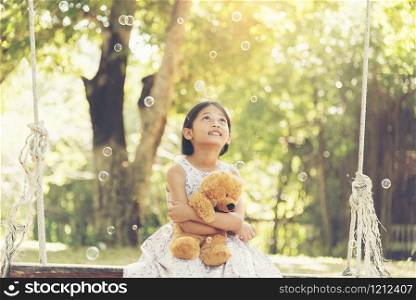 adorable happy cute girl sitting with teddy bear in the park