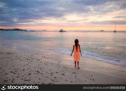 Adorable happy little girl on white beach at sunset. Sihouette of little girl dancing on the beach at sunset.
