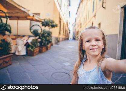 Adorable happy little girl taking selfie outdoors in european city. Portrait of caucasian kid enjoy summer vacation in old city. Adorable fashion little girl outdoors in European city