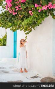 Adorable kid at street of typical greek traditional village with sea view on Mykonos Island, in Greece. Cute girl in blue dresses having fun outdoors on Mykonos streets