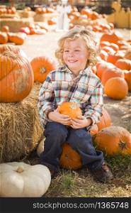 Adorable Little Boy Sitting and Holding His Pumpkin in a Rustic Ranch Setting at the Pumpkin Patch.