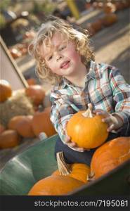 Adorable Little Boy Sitting in Wheelbarrow and Holding His Pumpkin in a Rustic Ranch Setting at the Pumpkin Patch.