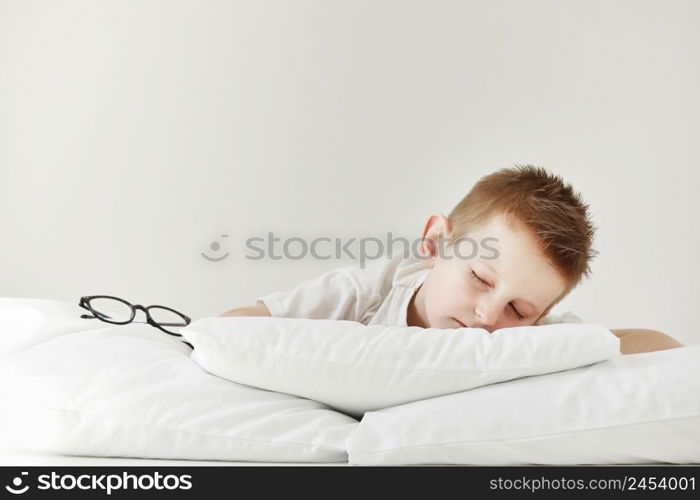 Adorable little boy sleeping in bed. morning dreaming on white bed. glasses from the side.. Adorable little boy sleeping in bed. morning dreaming on white bed. glasses from the side