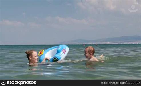 Adorable little boy swimming with his mother in the sea as she holds a small inflated lilo to support him