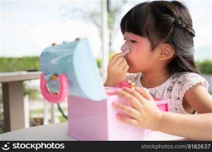 Adorable little child Asian girl paints her mouth with pink children heads and looks in the mirror. A child plays at home in a toy beauty salon. Increase learning development for preschoolers.
