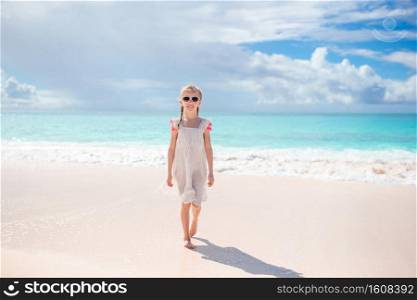Adorable little girl at beach having a lot of fun in shallow water. Happy kid looking at camera background beautiful sky and sea. Adorable active little girl at beach during summer vacation