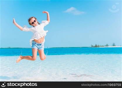 Adorable little girl at tropical beach on vacation splashing in shallow water. Adorable little girl have fun at tropical beach during vacation