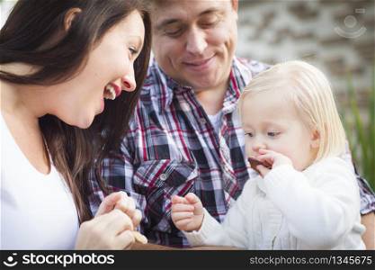 Adorable Little Girl Eating a Cookie with Mommy and Daddy Outside.