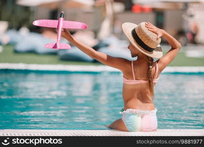 Adorable little girl have fun near outdoor swimming pool with toy plane in hands. Beautiful little girl having fun near an outdoor pool