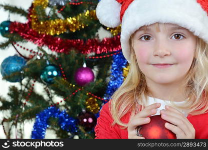 adorable little girl holding christmas ball near Christmas fir-tree