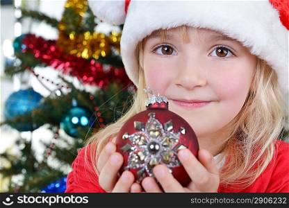 adorable little girl holding christmas ball near Christmas fir-tree