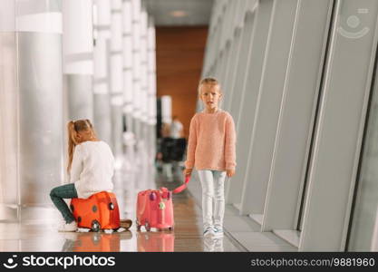 Adorable little girl in big international airport ready for vacation. Adorable little girls having fun in airport sitting on suitcase waiting for boarding