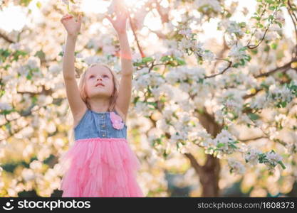 Adorable little girl in blooming apple garden on beautiful spring day. Cute girl in blooming apple tree garden enjoy the warm day