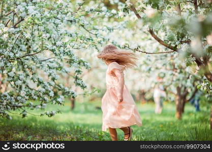 Adorable little girl in blooming apple garden on beautiful spring day. Cute girl in blooming apple tree garden enjoy the warm day