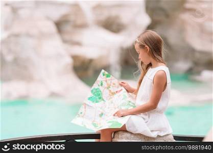 Adorable little girl looking at touristic map near Trevi Fountain, Rome, Italy. Happy toodler kid enjoy italian vacation holiday in Europe.. Young beautiful girl near fountain Fontana di Trevi with city map
