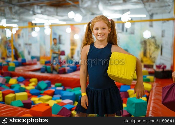 Adorable little girl playing with soft cube, playground in entertainment center. Play area indoors, playroom. Adorable little girl playing with soft cubes