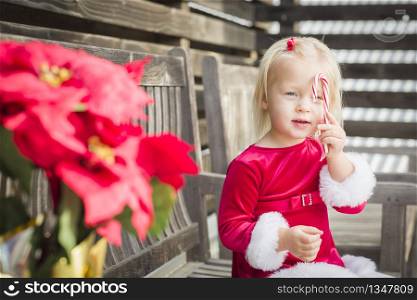 Adorable Little Girl Sitting On A Bench with Her Candy Cane Outside.