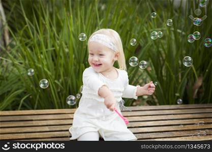 Adorable Little Girl Sitting On Bench Having Fun With Bubbles Outside.