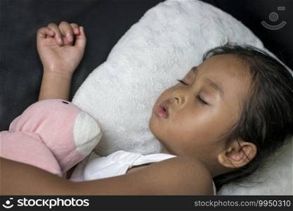 Adorable little girl sleeping with favorite toy on black sofa.