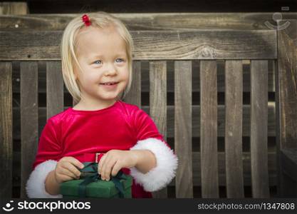 Adorable Little Girl Unwrapping Her Gift on a Bench Outside.