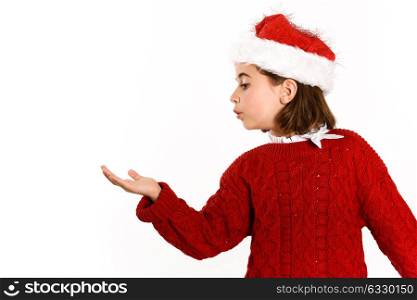 Adorable little girl wearing santa hat blowing to her hand on white background. Winter clothes